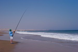 man fishing with a long fishing rod from a beach